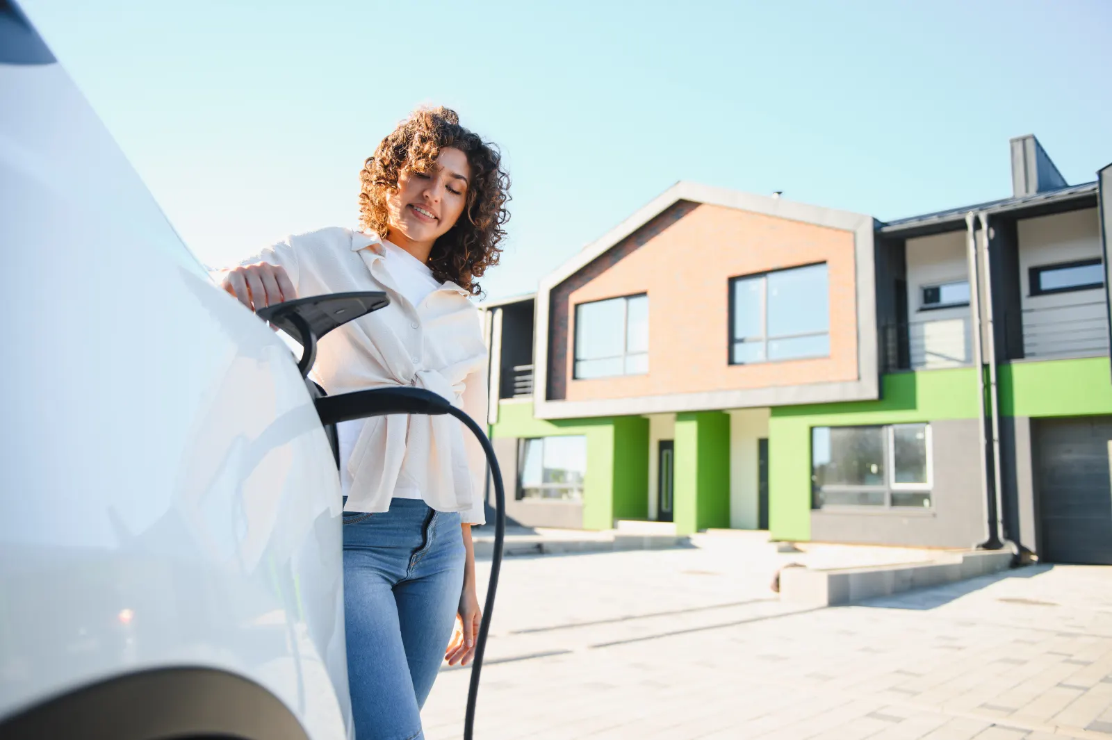Mujer cargando su coche eléctrico con un cargador instalado frente a su vivienda